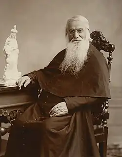 A bearded Sorin sits in a chair at a desk looking at the camera