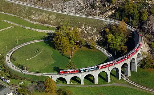 A train moving atop a stone bridge in an attractive valley