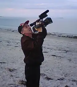 Photograph of Richard Dindo with camera, on a beach at Plymouth, Massachusetts, USA, while directing the film Mars Dreamers