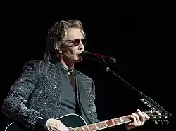 Springfield playing acoustic guitar, seated in front of a microphone