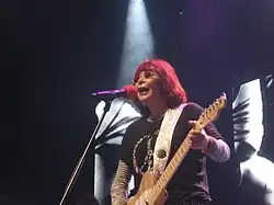 A woman singing and playing an electic guitar on stage.