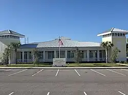 Daytime photo of the Riverview Public Library. It has an American flag on a pole in the middle. The building is a light yellow with yellow trim.
