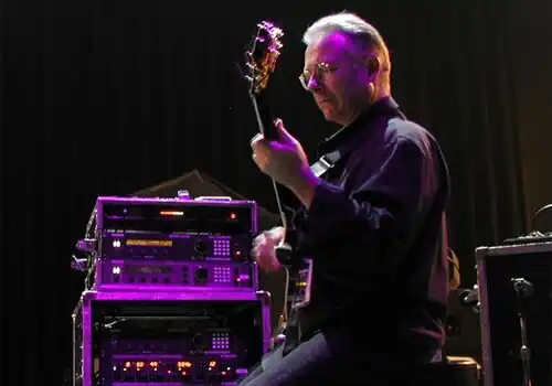 Robert Fripp ergonomically plays electric guitar while sitting in a posture developed through years of application of the Alexander Technique.