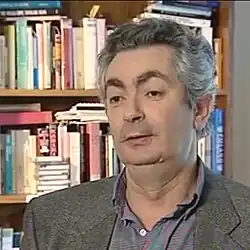 A man in a suit sitting in front of a bookshelf