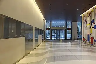 View of the lobby, facing south toward 50th Street, along the passageway on the eastern side of the elevator core. There are white and gray pavers on the floor. To the right is a wall with the artwork "Relational Painting No. 88", a multicolored art piece with geometric shapes.