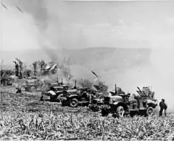 A row of trucks firing rockets, a cloud of dust is behind them.