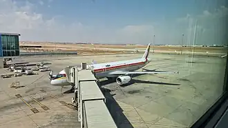 A Royal Jordanian passenger jet parked at a gate at Queen Alia International Airport in Amman, connected to a jet bridge.