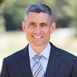 Color photograph, from the waist up, of a man wearing a suit and tie