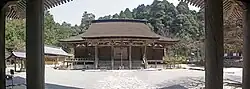 Enclosure of a sanctuary. There is an ablution pavilion, the main wooden building with a thatched roof and a three-storey pagoda. In the background,