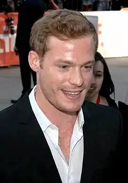 Sam Reid in a black suit talking to someone, taken from 45-degree angle