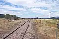 Looking east along the railway line from level crossing on Bylong Valley Way near Sandy Hollow, showing rear end of train waiting on crossing loop