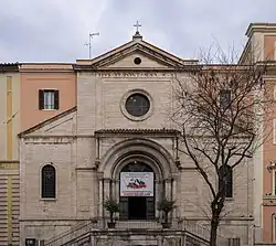 A beige stone building with a cross on top and a banner in the entrance.