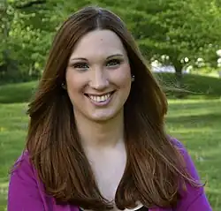 A portrait of Sarah McBride taken in 2016. She is wearing a fuchsia-colored sweater and is smiling.