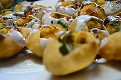 Small balls of thin dough are cracked open for a filling and topped with yoghurt.