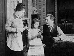 Black and white film still showing three people in period dress