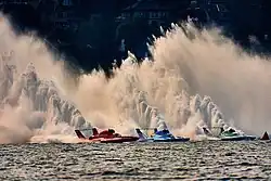 Three hydroplanes move alongside each other spewing tall sprays of water behind them