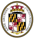 An oval seal featuring a shield with heraldic symbols