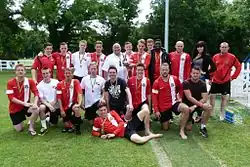 A group of 21 people in a football field. Most of them are wearing red and white jerseys depicting the coat of arms of Sealand.