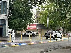A worker dressed in white jacket, pants, and hat stands on the mural's second T and uses a hose to wash the paint. The hose is attached to a white maintenance truck parked on top of the mural.