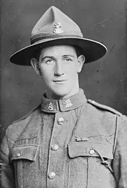 A studio portrait of a man in military uniform. He is wearing a hat, and has a medal ribbon on his breast.