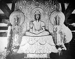 Image 66Shakyamuni Triad by Tori Busshi depicts the Buddha Shakyamuni in the traditional sixth-century Chinese style with an elongated head and in front of a flaming mandorla – a lotus petal shaped cloud. (from Buddhist art in Japan)
