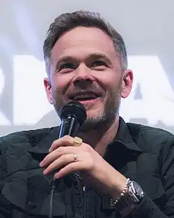 Shawn Ashmore smiling as he sits at a microphone