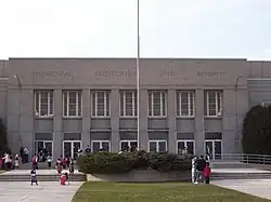 The entrance of a concrete building behind a front lawn and a flag pole