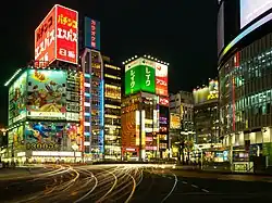 Brightly lit and colourful buildings at night in Tokyo, with car light trails in the foreground.