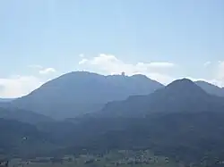 A forested landscape of low mountains, with the profile of a domed building on a distant ridgeline
