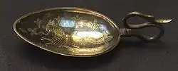 a short-handled spoon with fine detail marked in the bowl of the spoon of a cat-headed fish-tailed creature surrounded by fleur de lys
