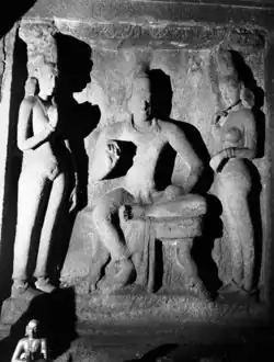 A stone relief carving showing a seated king with two queens standing beside him.