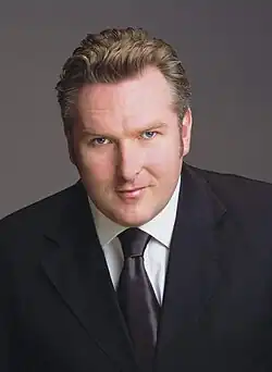 Man with short, brown hair wearing a black suit.