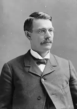 Head of a 40sh man with gray hair, squinting through eyeglasses