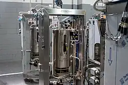 A stainless steel single-use bioreactor system, featuring integrated sensors and tubing, located in a Factory Acceptance Testing (FAT) room.