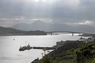 A narrow sea inlet with a shipping terminal and a large bridge