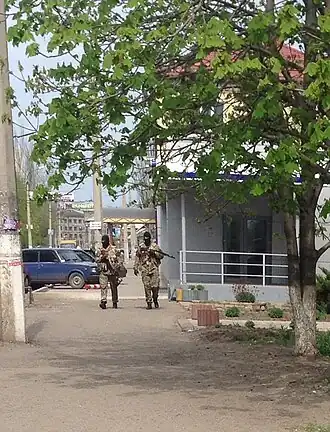 Two armed, amsked soldiers walking down a street