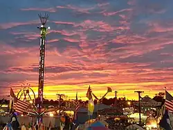 A state fair with a setting sun and clouds in the background