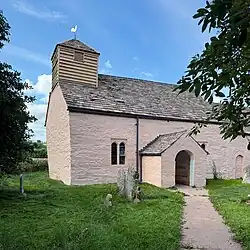 A pink-washed stone church with a wooden bell Cote and a central porch