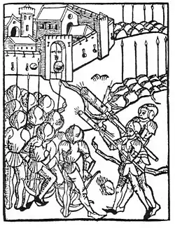 Black-and-white woodcut showing armed soldiers outside a walled medieval city; several figures aim long pole-mounted firearms toward the gate while others stand clustered nearby, with towers, walls, and rooftops in the background.