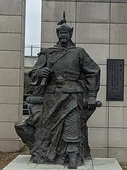 A color photograph of a black stone statue of a man in Chinese medieval military costume