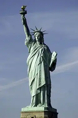 A crowned, robed woman holding aloft a torch
