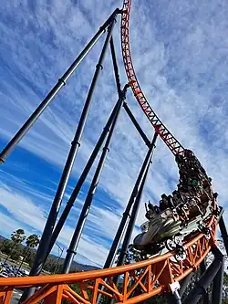 Orange rollercoaster descending through a twisted spike element.