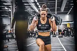 Lauren Weeks, a muscular white woman, competing in Hyrox in a lunge carrying weights on her back