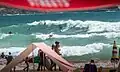 Surfers and beachgoers on a busy summer day