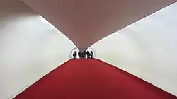 Interior of a flight tube, a hallway with rounded white walls, a white ceiling, and a red carpet