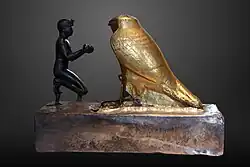 Taharqa offering wine jars to Falcon-god Hemen;[77] 690–664 BC; bronze, greywacke, gold and wood; length: 26&nbsp;cm, height: 19.7&nbsp;cm, width: 10.3&nbsp;cm; Louvre