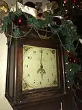 A grandfather clock in the foyer, adorned for the winter holidays