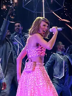 Taylor Swift singing on a microphone, wearing a polka-dot pink two piece dress