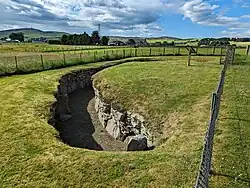 Uncovered underground passage with stone walls in a grassy field