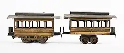 Two antique model train cars. Each car has a single truck (cluster of four wheels) in the center of the car.